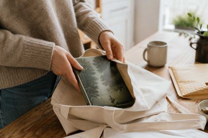 A reader sliding a hardback into a cloth bag, a padded envelope on the table beside it